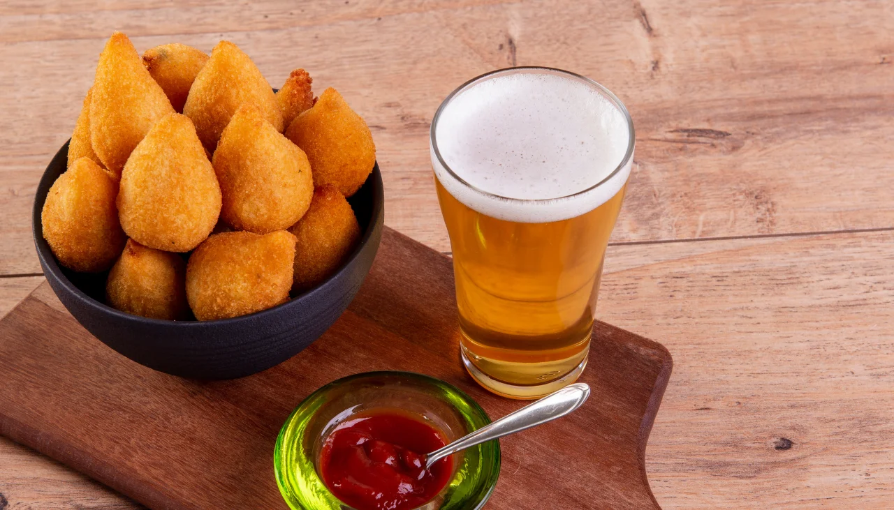 Coxinha servida com cerveja e molho de ketchup.